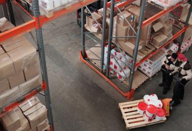 Palletised goods on warehouse racking with two workers moving a pallet, cargo sitting in a forwarder's custody